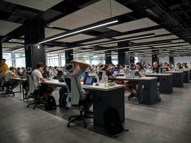 Shot of an open office setting with dozens of workers sitting at desks on laptops.