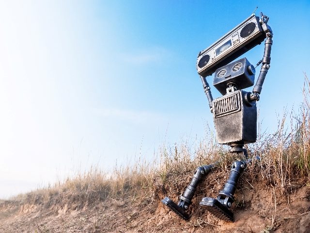 Robot on a background of blue sky, holding up a radio, symbolizing how brands need to ensure AI has a voice that is consistent with the brand's.