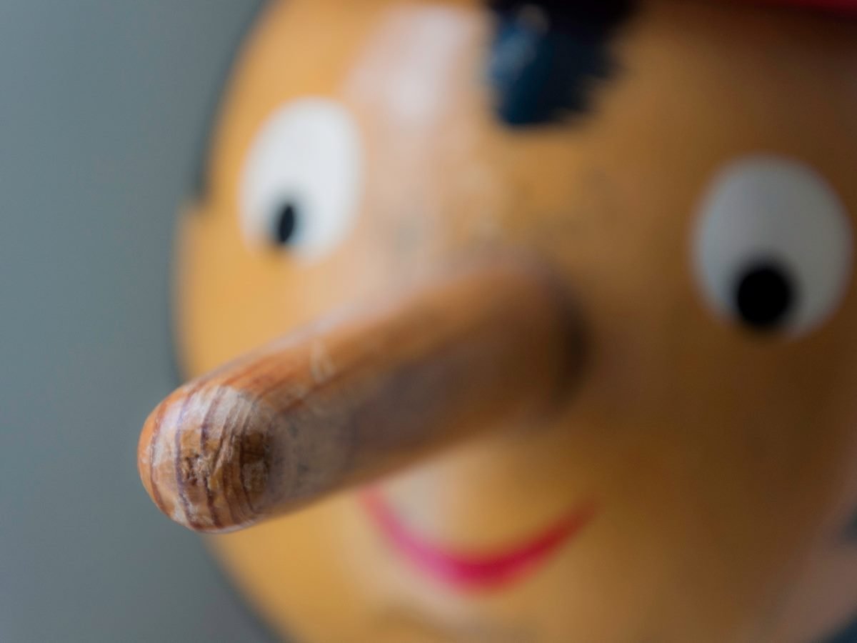 Close-up of a wooden Pinocchio puppet, focusing on its long nose and smiling face, symbolizing dishonesty or exaggeration.