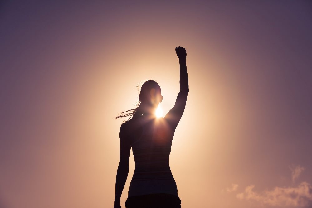 The silhouette of a person raising their fist up into the air against a dramatic orange sky background in piece about customer empowerment.