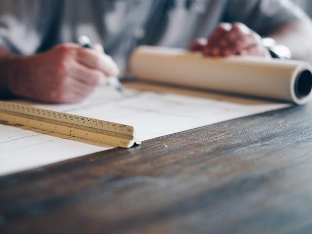 Someone's hand with a pencil in it analyzing blueprints.