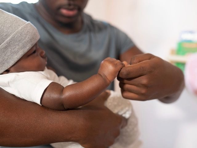 father holding his baby, offering a finger to  clutch