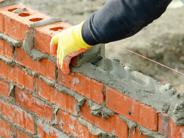 Bricklayer laying bricks on mortar on new residential house construction.