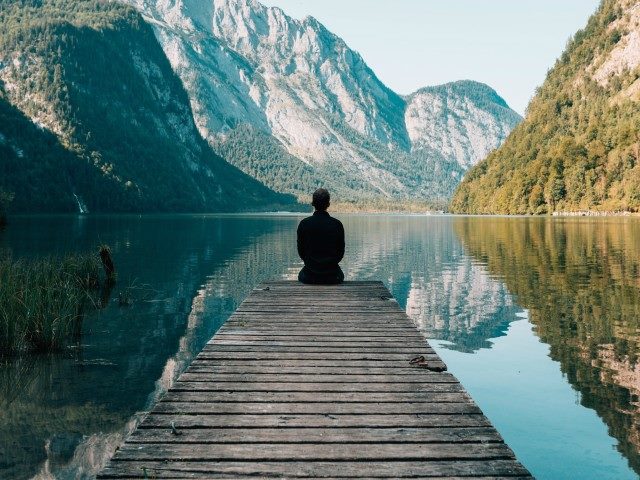 Person sitting at end of a dock overlooking a river between mountains.