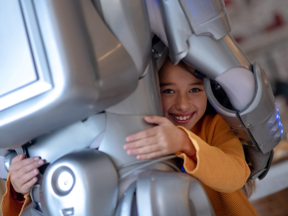 Child hugging a humanoid robot, smiling while interacting closely with the machine, illustrating human trust and emotional connection with AI.
