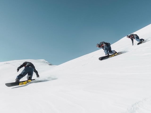 3 snowboarders accelerating downhill