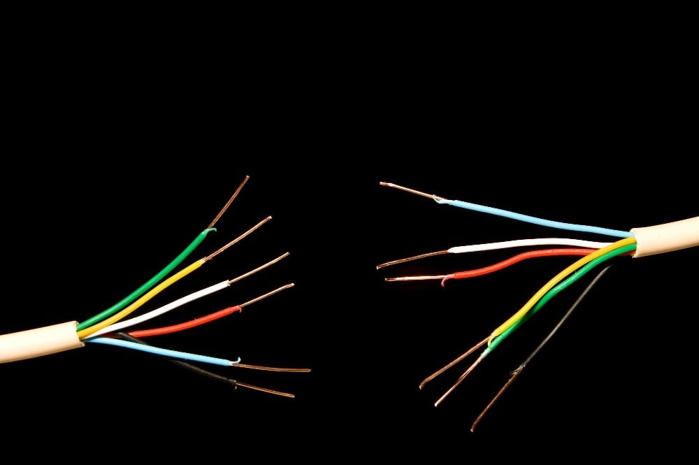 Two separate segments of a multi-colored electrical cable are depicted against a black background, symbolizing a disconnection or breakdown. The exposed wires in colors of green, yellow, blue, red, and brown represent the complexity and vulnerability of systems affected by the CrowdStrike software failure, emphasizing the need for effective crisis management in IT.