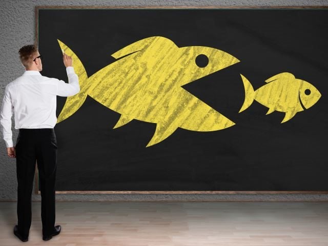 A businessman drawing a sketch of a big fish eating a small fish - competitive advantage concept