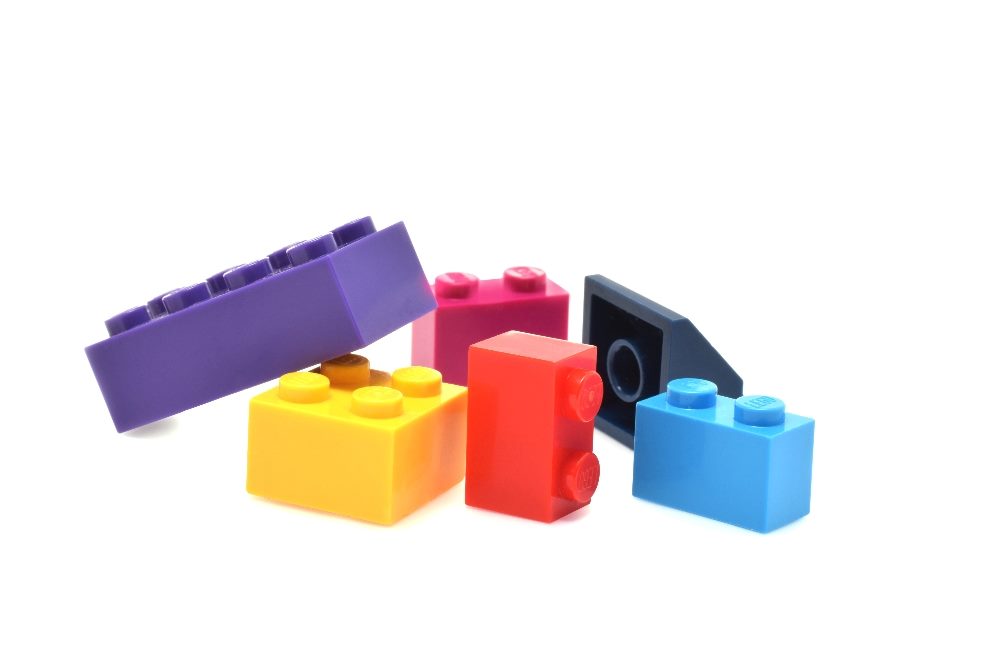 Colorful Lego blocks, including purple, blue, yellow, red, black, positioned in a group against a white background in piece about customer experience strategies.