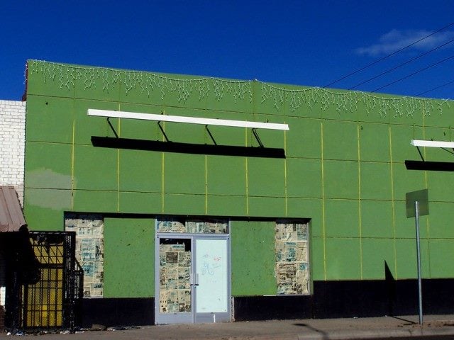 A green-painted building with newspapers covering up some windows.