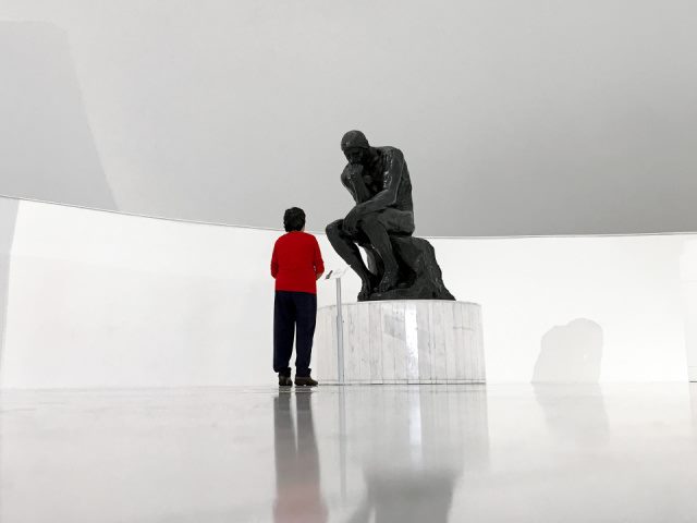 person in red jacket and black pants looking at the thinker statue