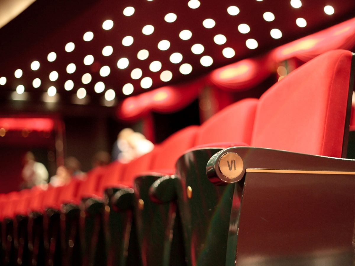 Empty red theater seats under warm marquee lighting, symbolizing the idea of “feedback theater” where appearances can mask what is really happening behind the scenes.