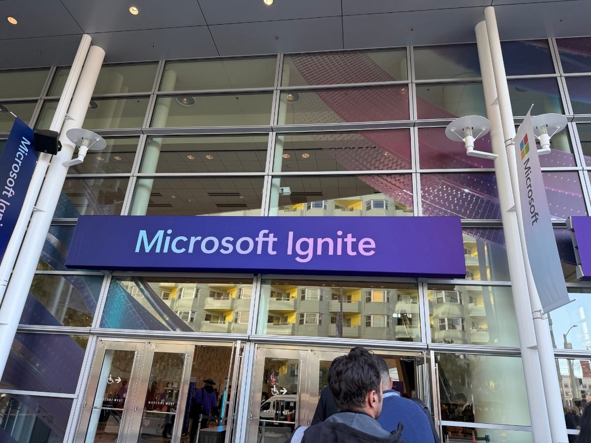 Attendees enter the main entrance of Microsoft Ignite, marked by a large purple sign above the doors and flanked by Microsoft-branded banners.