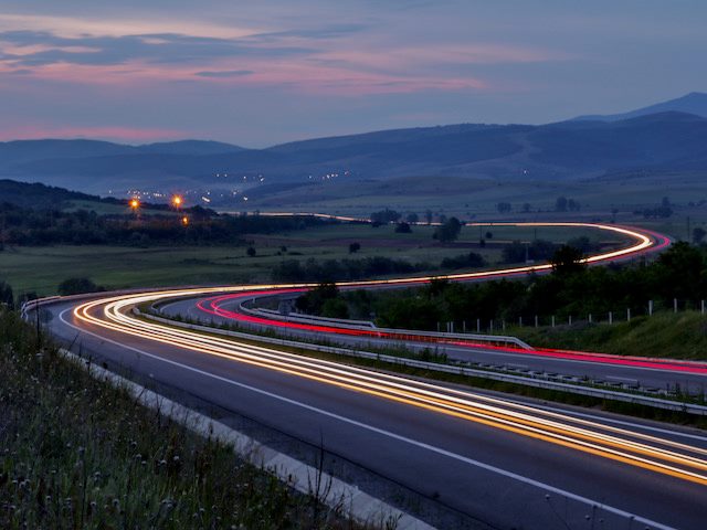 cars speeding down  a highway at dusk,  lights on