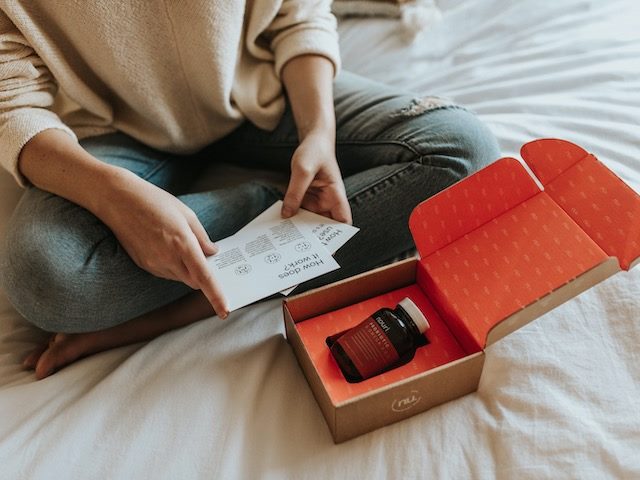 woman sitting  on  her  bed looking at literature from a vitamin delivery