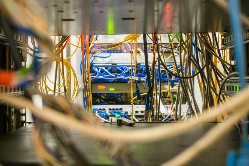 Communication cables and fiber optic patches are visible in a switching cabinet of an internet provider in piece about AIOps for customer service issues with the Amazon Just Walk Out technology.