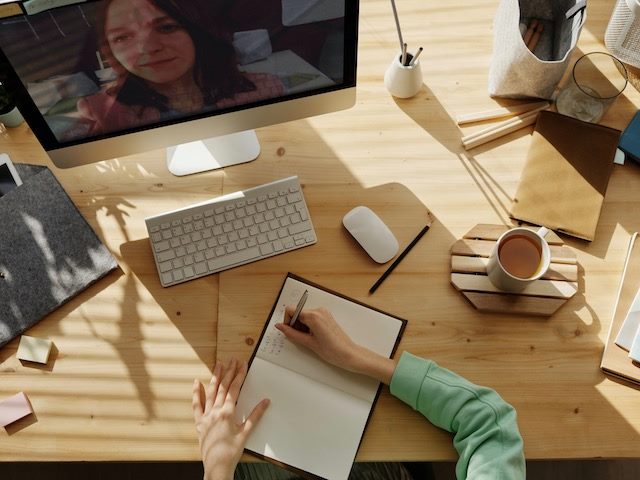 person taking an online training course, writing notes in a notebook
