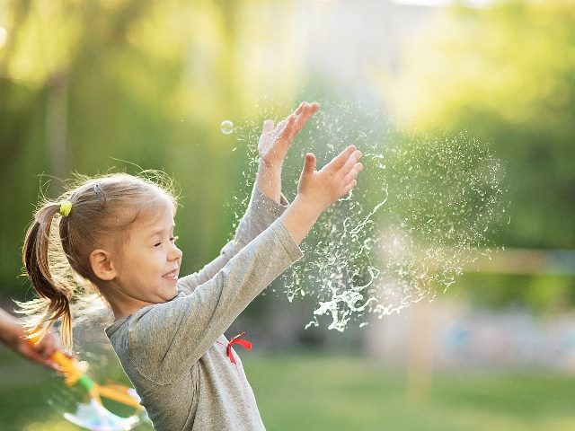 Portrait of happy and active little girl bursting soap bubbles. 