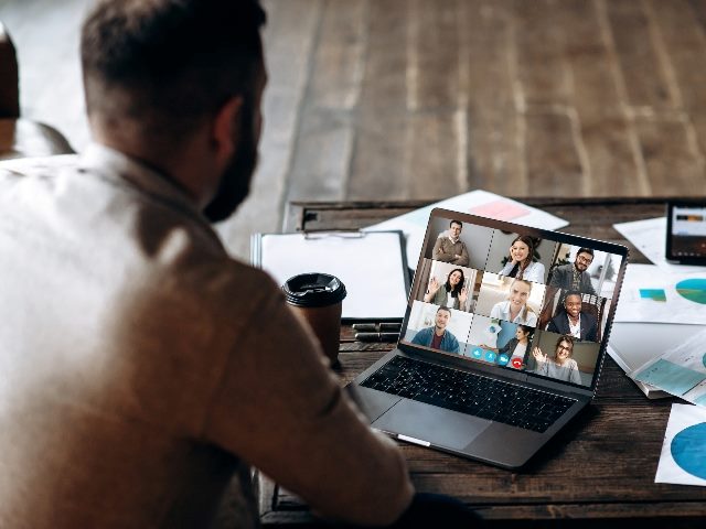 Young bearded man communicates via video call with colleagues, as he sits at the creative modern office space.  