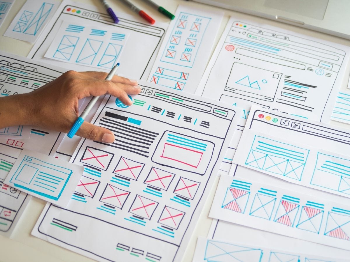 Hand sketching website wireframes on paper, showing page layouts, content blocks and navigation elements during the design planning process.