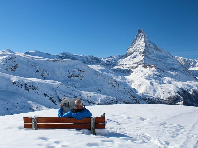 A man on a park bench on a snowy mountaintop, reading the newspaper - news concept