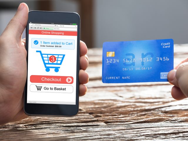 A customer completing an online purchase on his mobile card. Holding a credit card in one hand and a phone in the other.