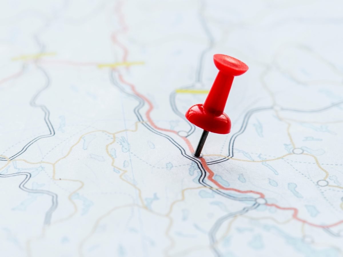 A close-up of a paper map with a red pushpin marking a specific point along a highlighted route.