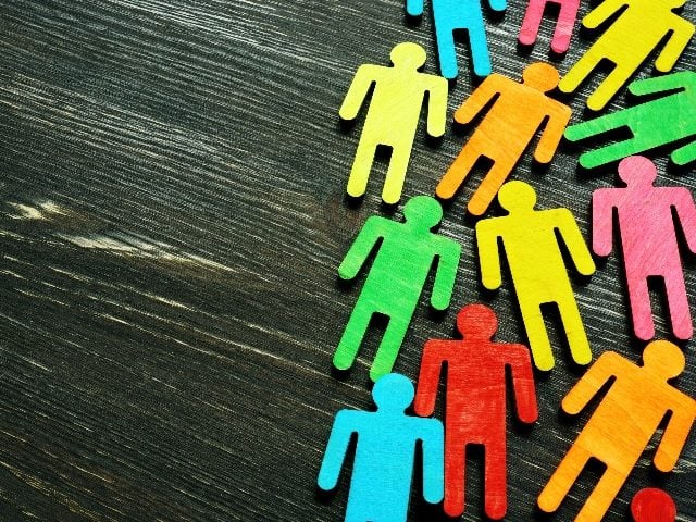 Diversity and inclusion background with wooden, colored stick figures on dark wooden desk. 