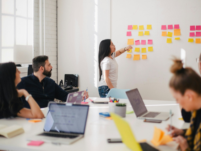 A group of people using laptops and using sticky notes on the wall 