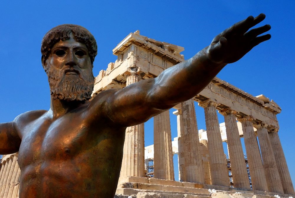 A bronze statue of Zeus with his arm pulled back as if throwing a spear in front off the Acropolis in Athens in piece about headless CMS versus monolithic CMS.