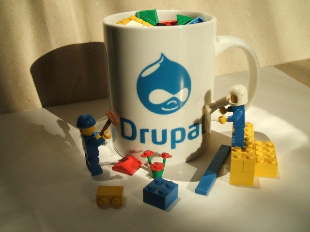 A coffee mug with Drupal written on it along with Drupal logo, surrounded by Legos.