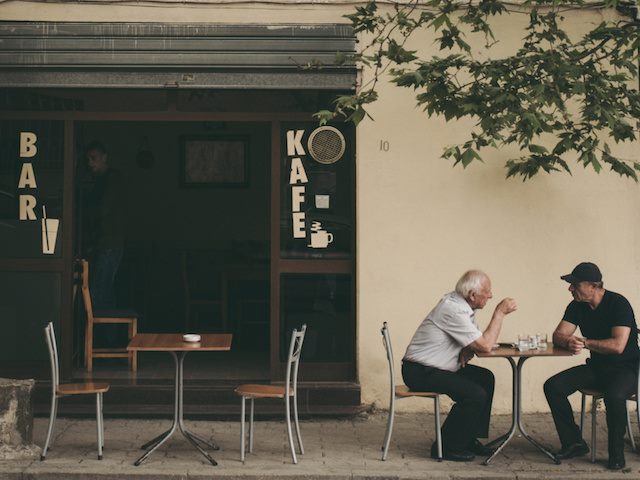two men having a conversation in front of a cafe
