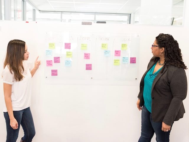 two women discussing ideas in front of a whiteboard