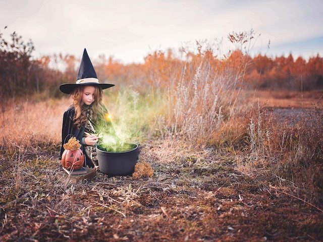 a little girl, dressed as a witch, making a spell in a caldron in the middle of a field