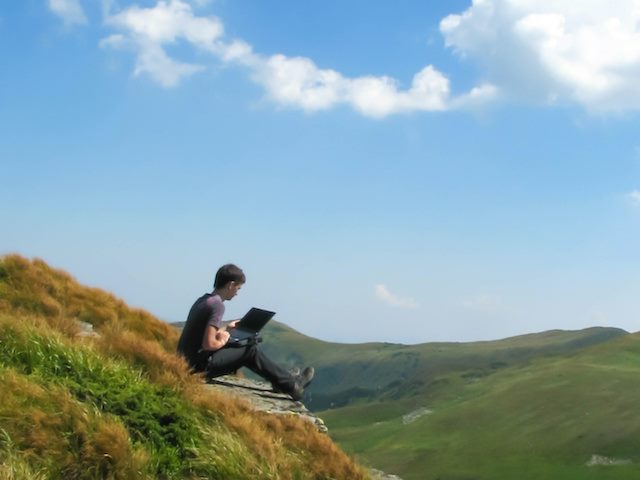 remote worker with laptop sitting on top of mountain