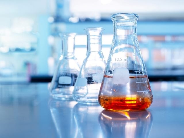 Orange solution in science glass flask next to two empty flask glasses, representing a science-based startup and the challenges of marketing science-based products and brands.