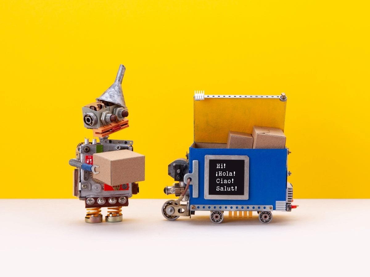 Toy-style robot handing a cardboard box to a small delivery cart robot with a multilingual screen (Hi, Hola, Ciao, Salut) against a bright yellow background, symbolizing AI-driven conversational commerce and automated transactions.