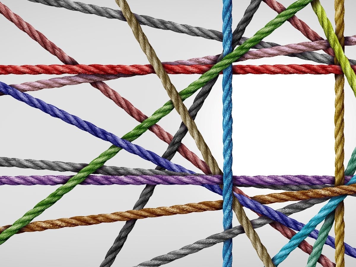 Multiple colorful ropes crossing and overlapping in different directions against a light gray background, visually representing interconnected systems, complexity, data dependencies and converging workflows.