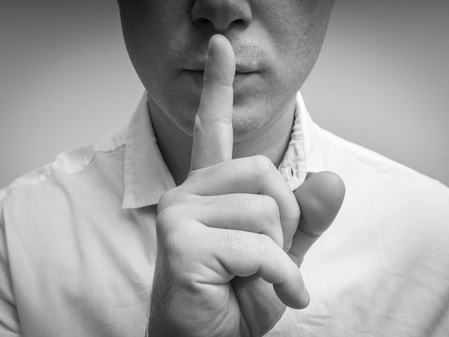 man with finger in front of his face making "shh" signal