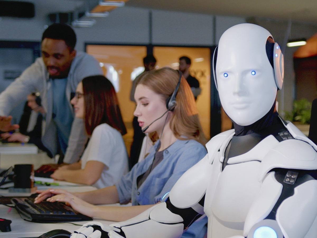 Concept image of a humanoid robot sitting alongside human call center agents, symbolizing AI-powered customer service working with people.