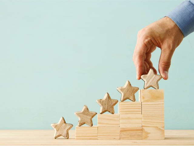 wood blocks arranged like a stairway with stars on each step and a hand placing one more star on top.
