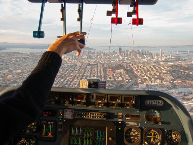 Image from the cockpit of a small airplane with pilot pointing toward and arial view of San Francisco