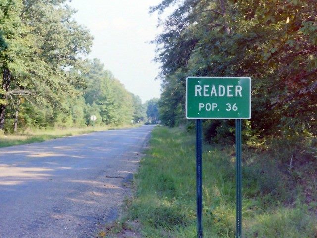 A sign that says "reader pop. 36" on a quiet road.
