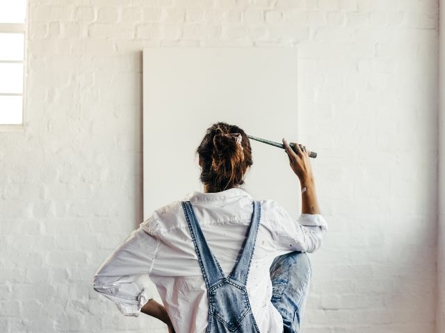 Female painter contemplating creative ideas for her new art project with a blank canvas in front of her. 