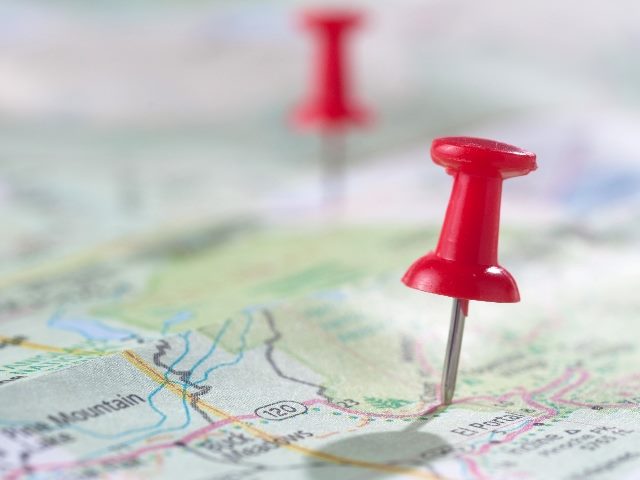 Two red pins pinned to a map, one pin in the foreground and one blurred out in the background.
