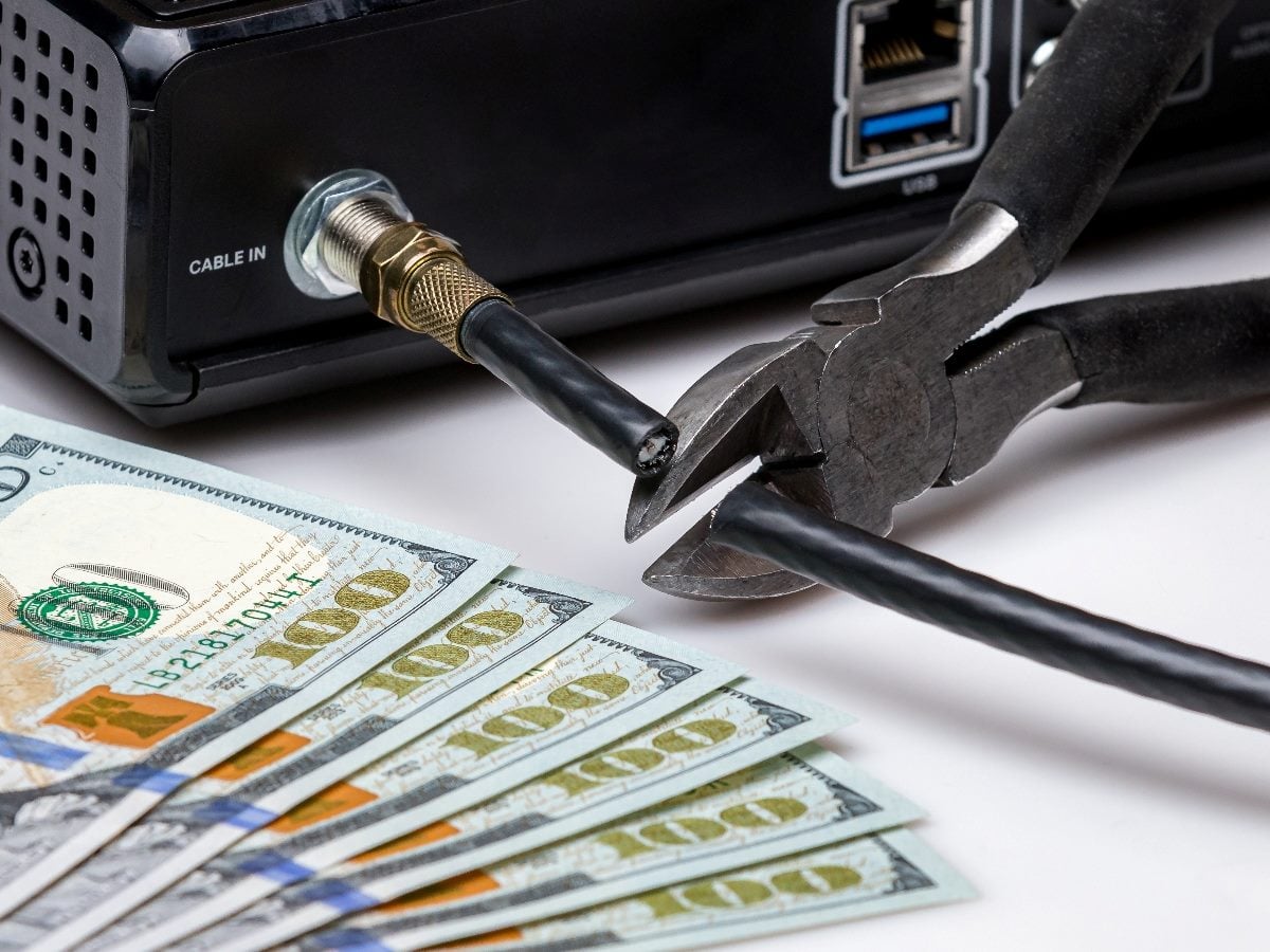 Close-up of a cable box with a coaxial cable being cut by pliers next to U.S. $100 bills, symbolizing cutting service costs or reducing expenses.
