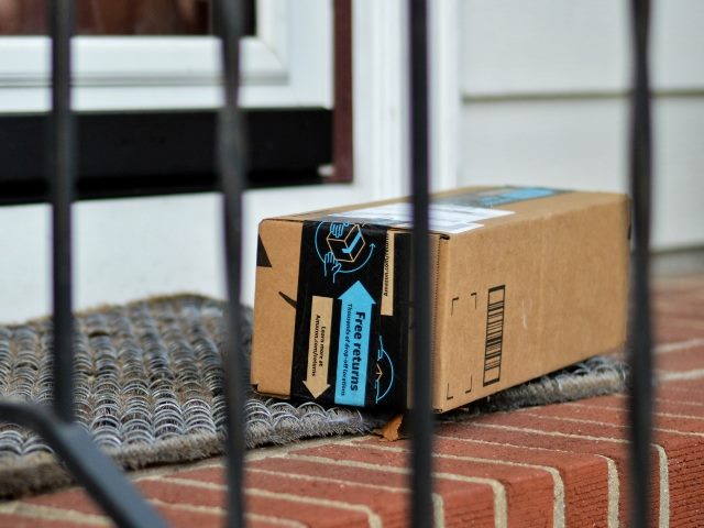 Amazon box shipped to a residential house as seen on a brick step through a steel staircase railing.