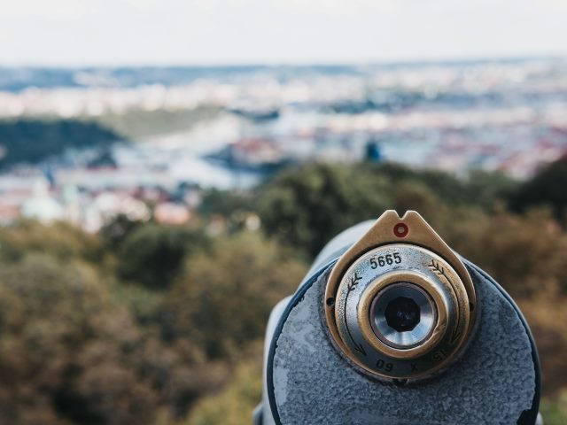 Coin-operated binoculars in the foreground, Petrin Tower, Prague, in summer, blurred in the background.