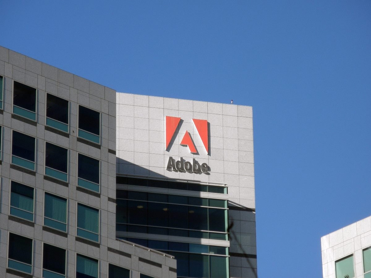 Exterior of an Adobe office building with the red Adobe logo and company name mounted on the facade against a clear blue sky.
