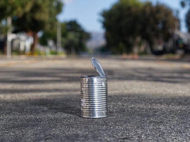 The image shows a silver, empty tin can with its lid partially detached and upright, sitting on a paved street. The background features a sunny, tree-lined suburban road with no visible traffic, possibly waiting to be kicked to the curb in pieces about customer data breaches and other data issues. 